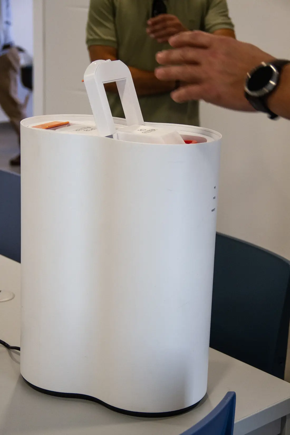 Dispensador de agua blanco con el asa del filtro levantada mientras una persona lo muestra
