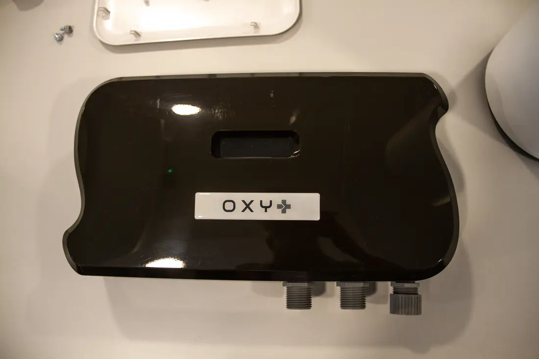 Equipo de tratamiento de agua OXY+ en negro, con sus conexiones a la vista junto a la placa de montaje